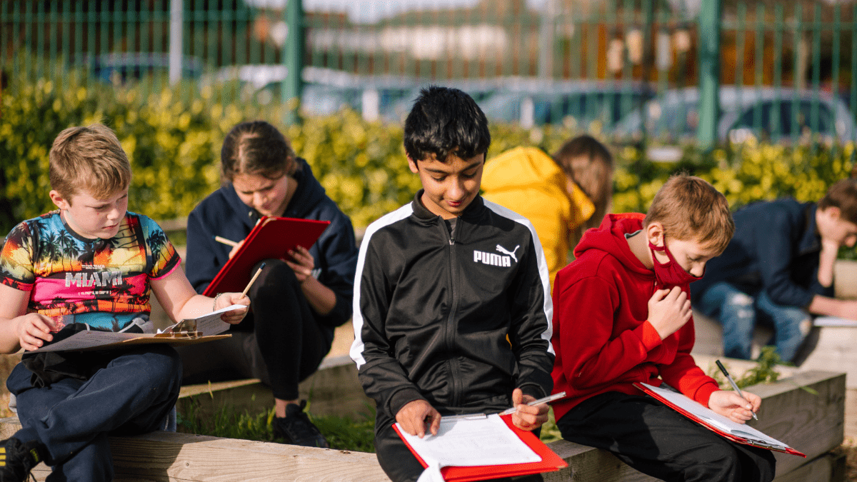 Teenagers working on clipboards in their school grounds during an activity with the My School, My Planet project run by Learning through Landscapes.