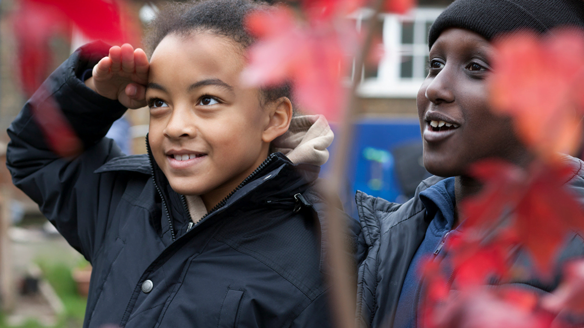 Two children laughing in their autumnal school grounds as they participate in an activity through the My School, My Planet project run by Learning through Landscapes.