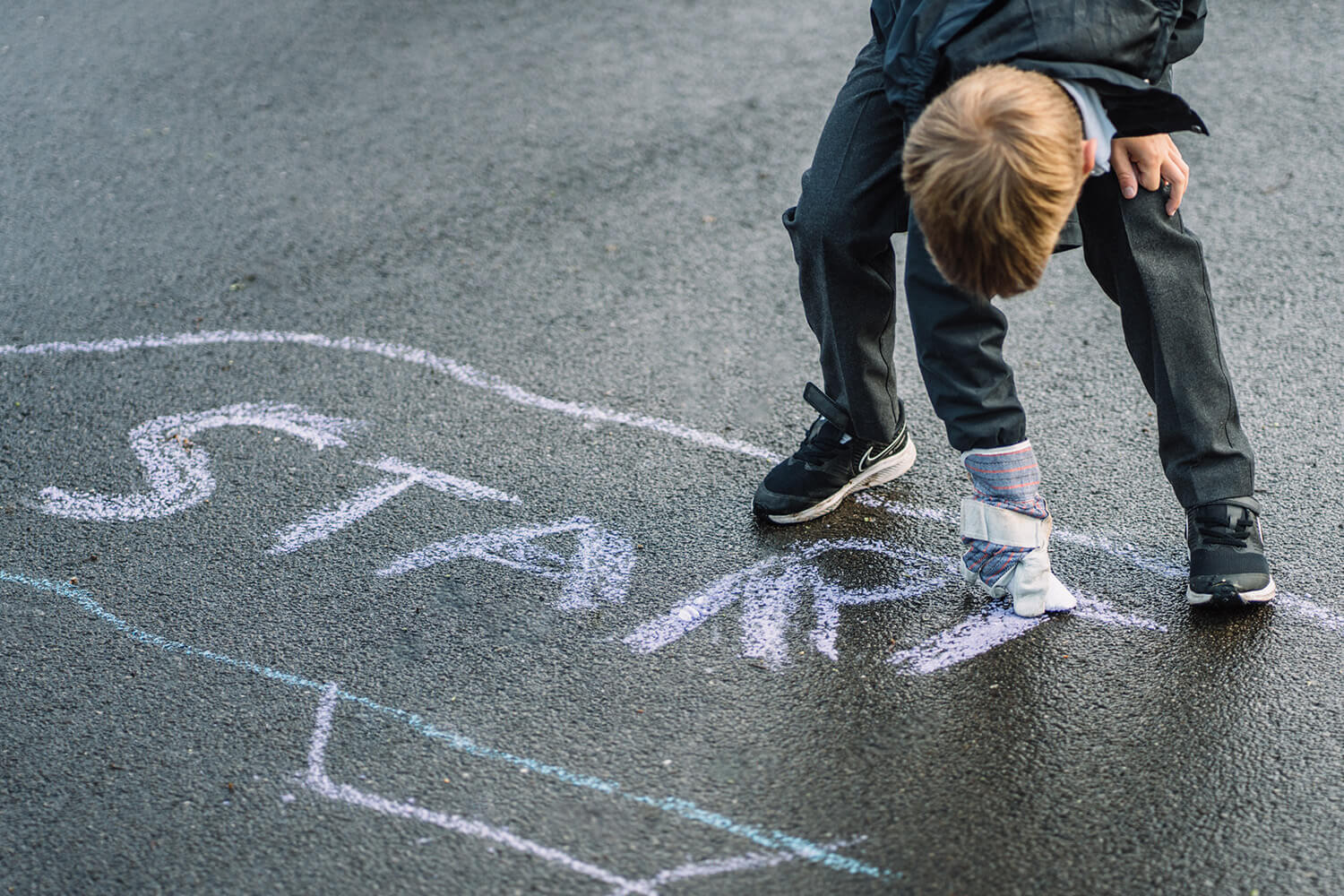A boy writing the word 'start' on the playground using chalk.