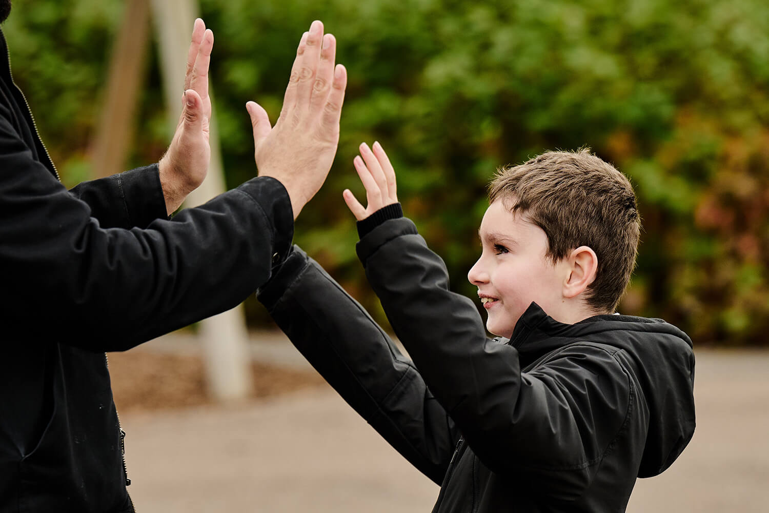 A child smiling as he gives a high-five to his teacher in an outdoor classroom.