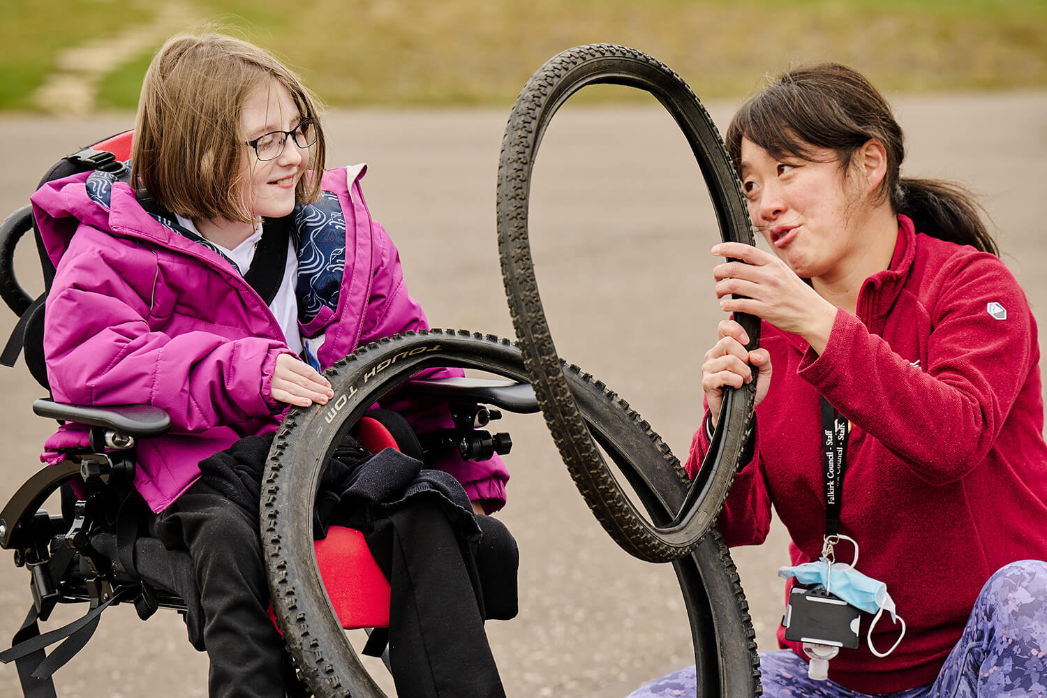 A teacher working with a pupil using bicycle tires in their outdoor classroom.