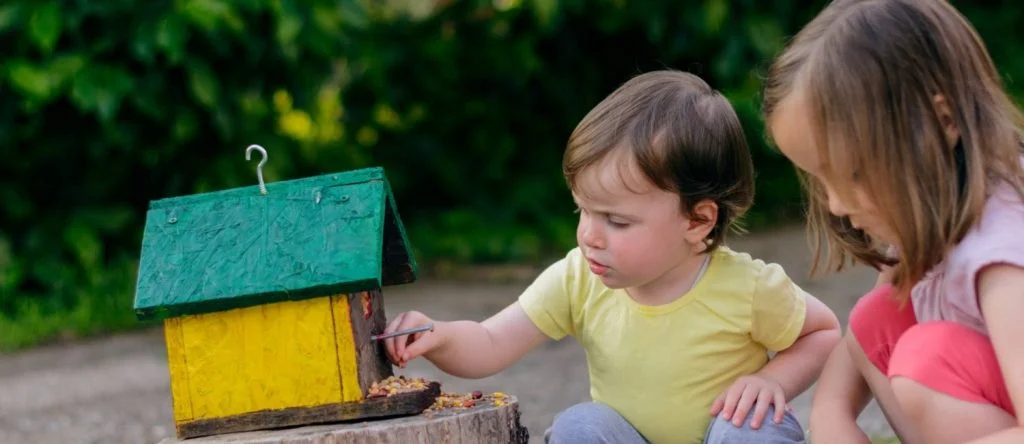 Two young children putting food into a birdhouse.