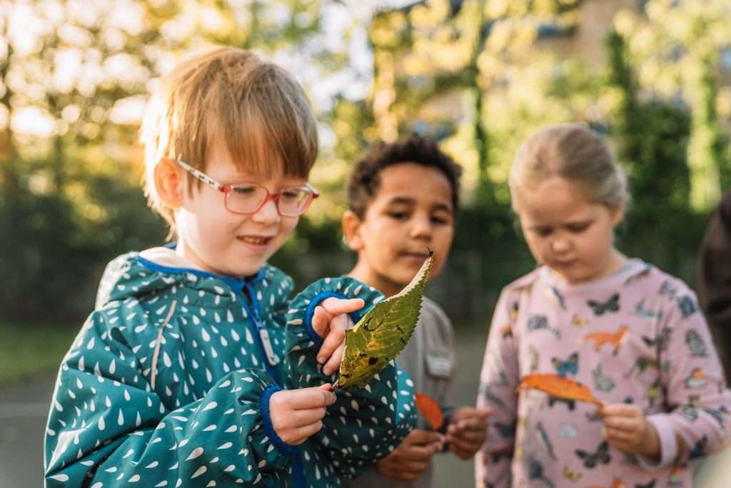 three children examine leaves in the playground