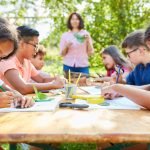 A teacher confidently guiding her young pupils through still life art in an outdoor classroom