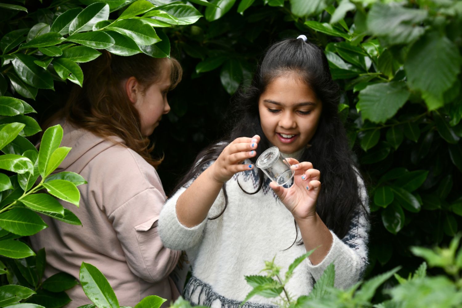 Two children examining an insect in a jar during an outdoor lesson on climate and sustainability.