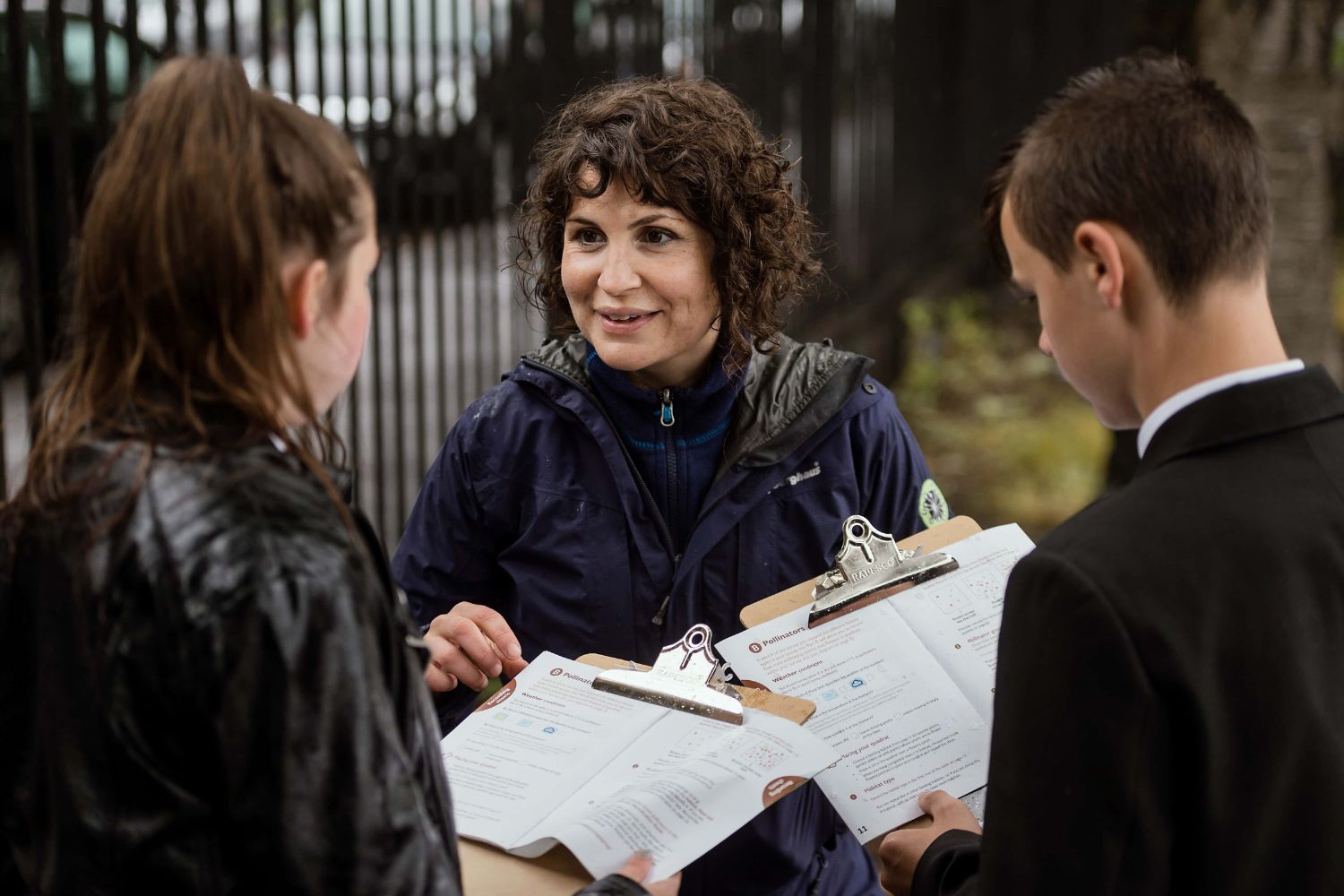 A teacher and two teenagers look at checklists on clipboards working together outdoors.