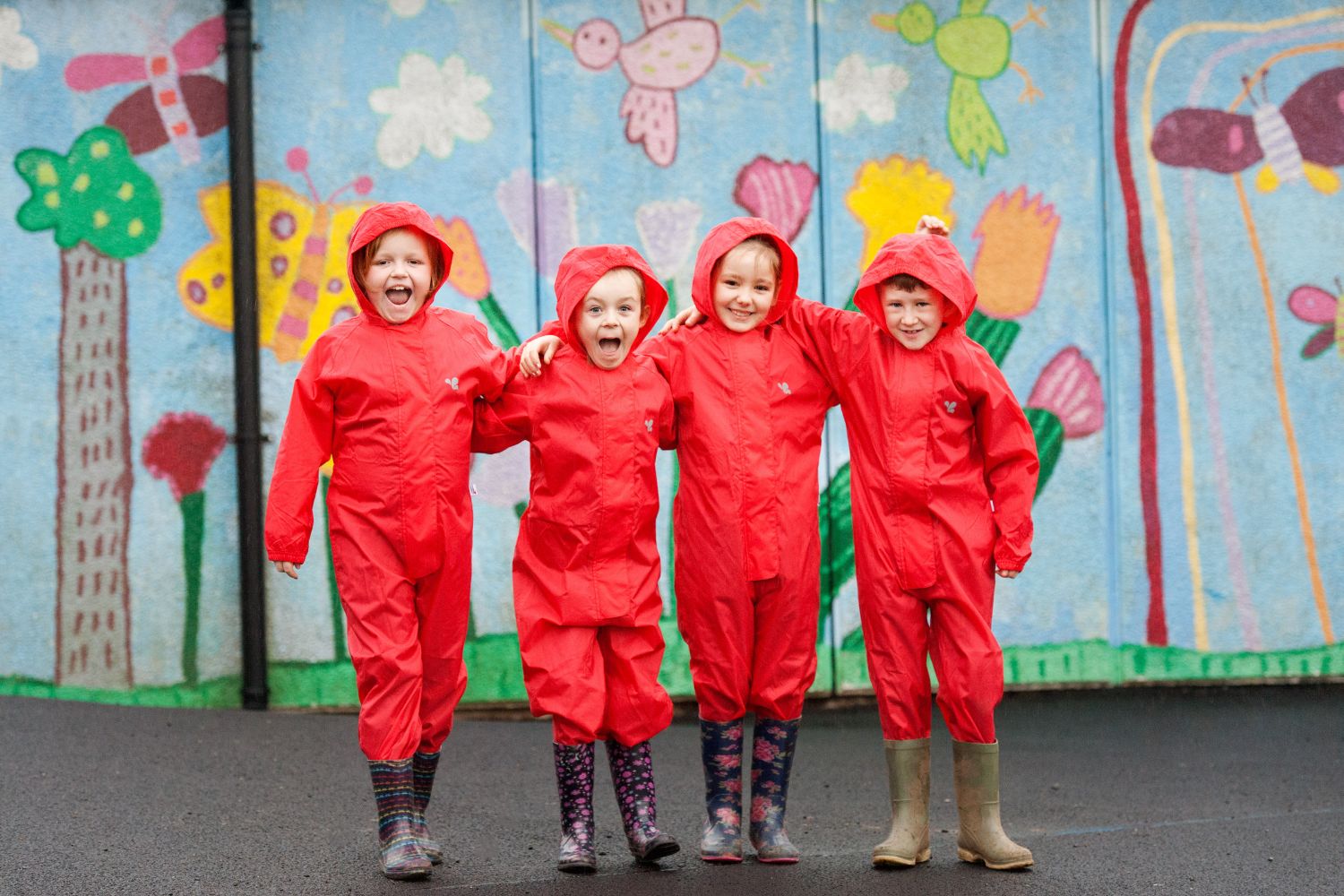 Children wearing bright red waterproof coveralls laughing in their rainy school grounds.