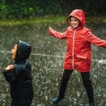 Children wearing wet weather clothing, laughing with delight as they play in their rainy school grounds.