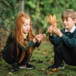 Two primary school children examining and sorting leaves during an outdoor lesson in their school grounds.