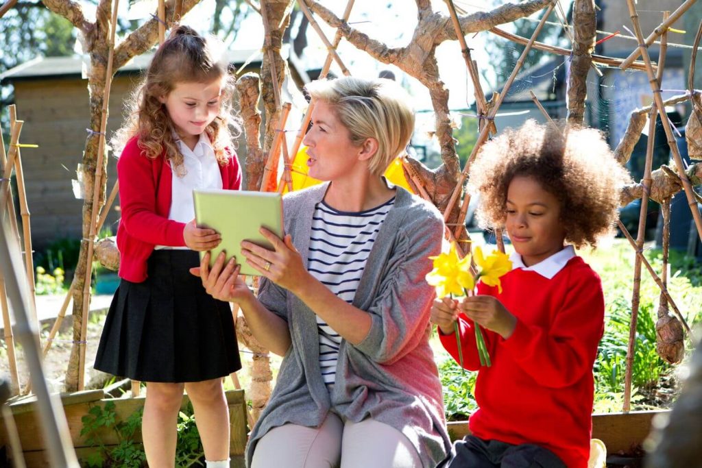 A teacher studying daffodils with her young pupils during an outdoor art lesson.