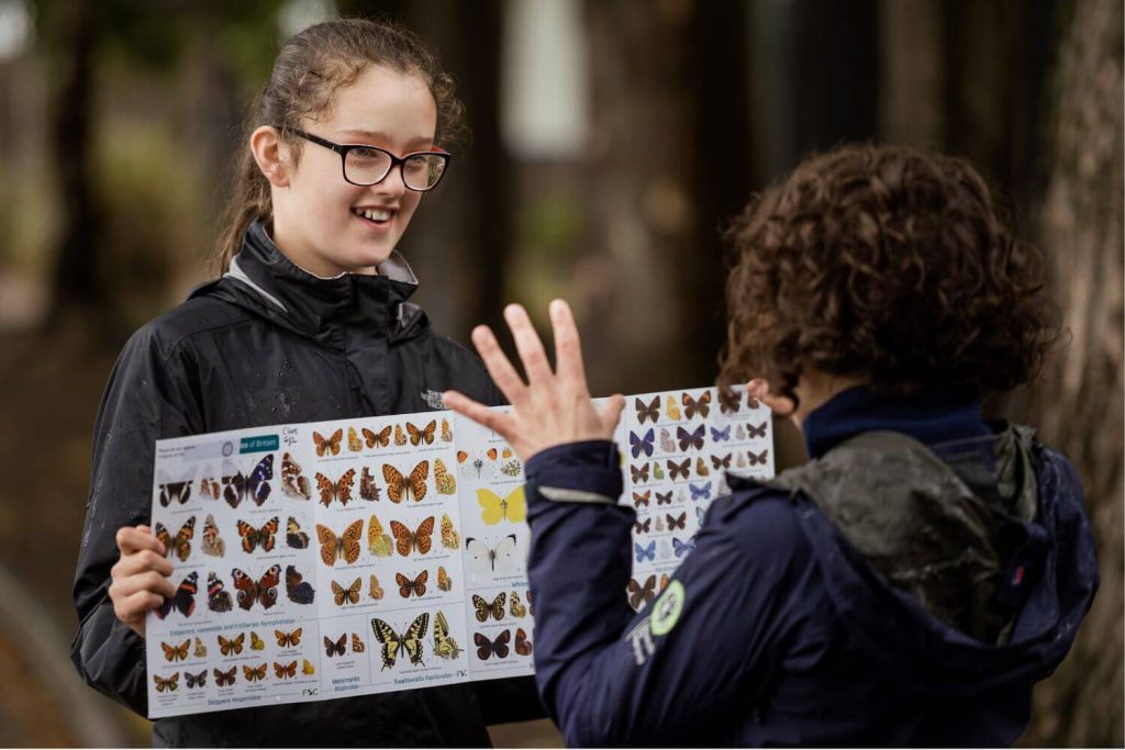 A secondary schoolgirl holding a poster of butterfly species as she discusses biodiversity in the school grounds with her teacher.