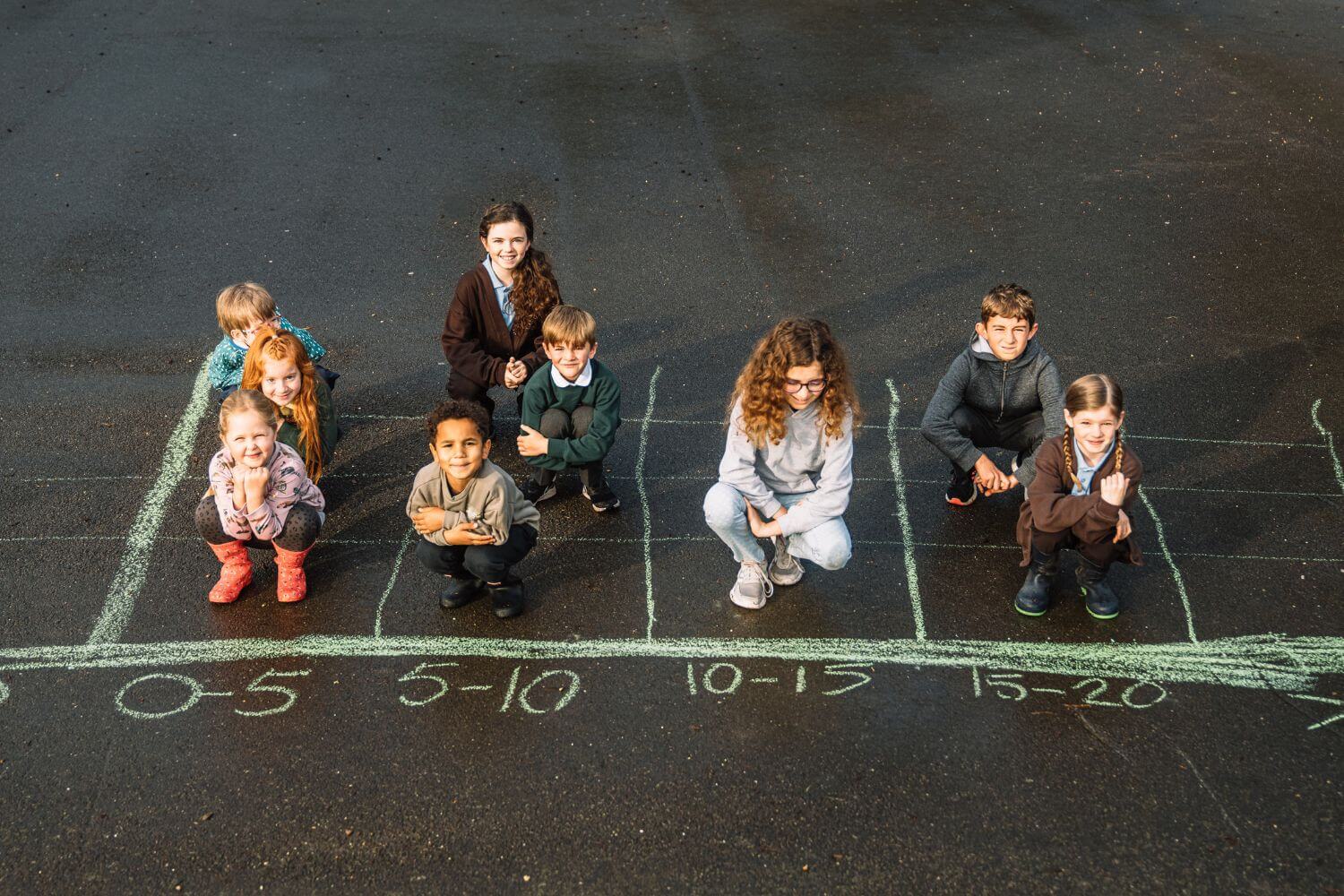 A group of primary school children in a number grid drawn out in chalk on the playground during an outdoor numeracy activity.