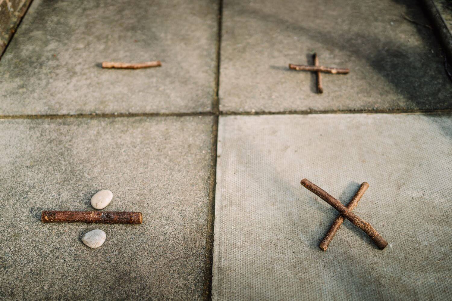 Mathematical symbols depicted on the school playground using natural materials like sticks and pebbles.