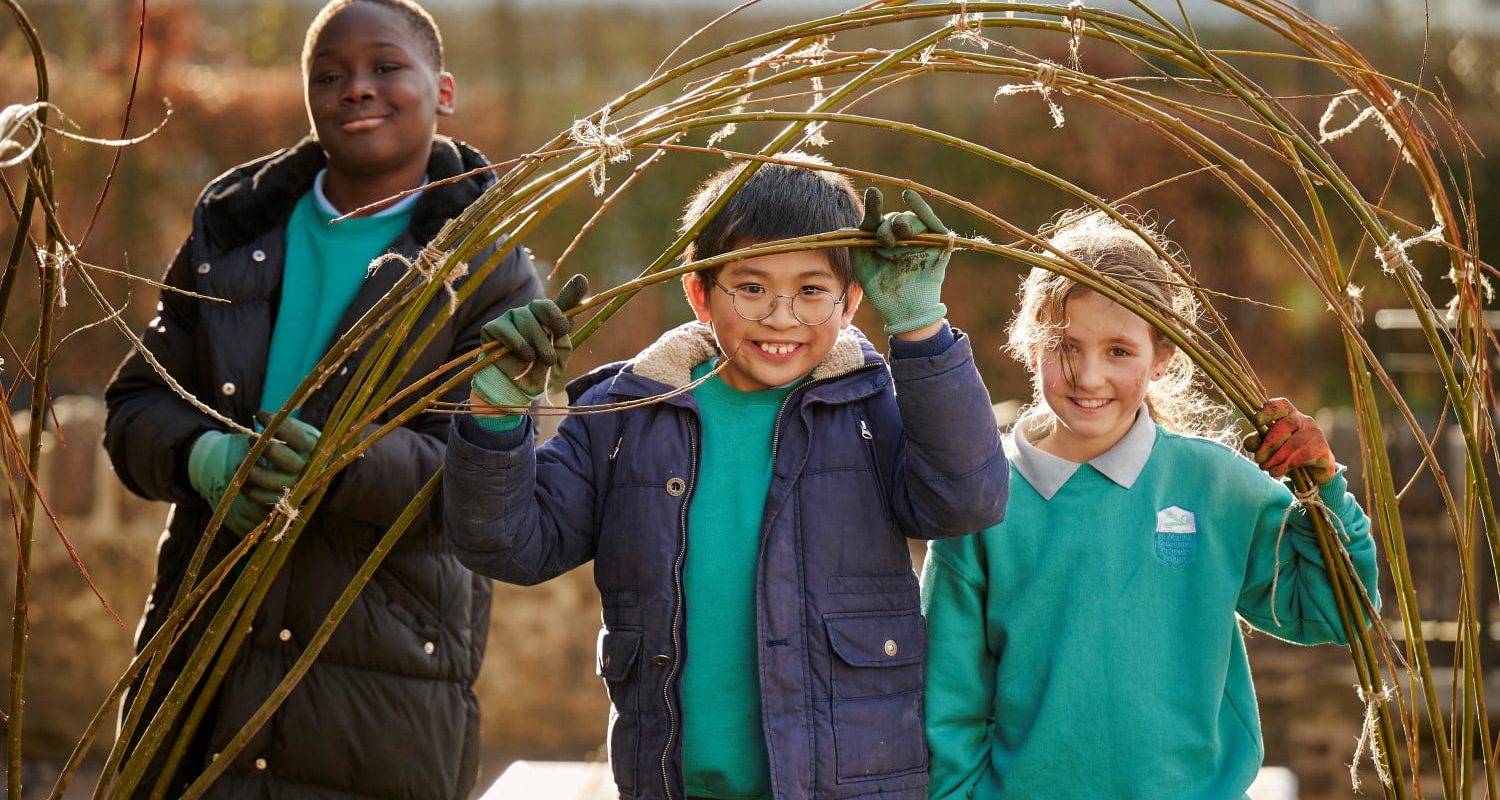 Children building a willow structure for plants to climb in their climate ready school grounds.