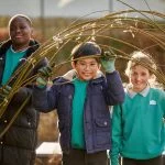 Children building a willow structure for plants to climb in their climate ready school grounds.