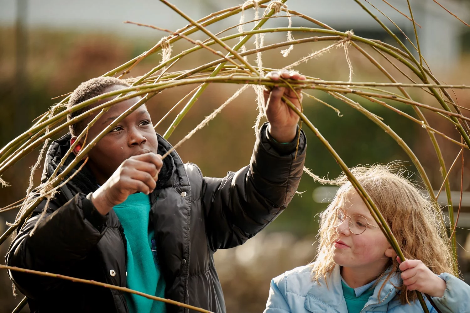 Children building a willow structure for plants to climb in their climate ready school grounds.