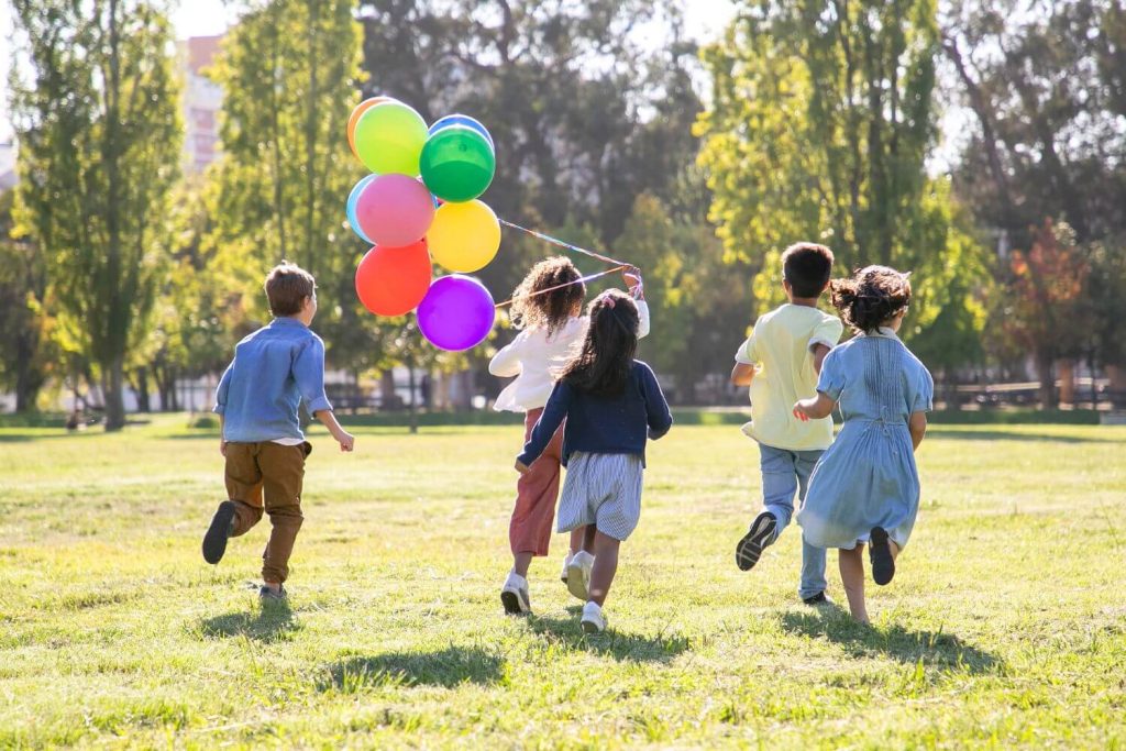 School children running across their grassy school grounds with a bunch of colourful balloons on Outdoor Classroom Day.
