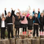 Group of children on tree stumps with their arms raised