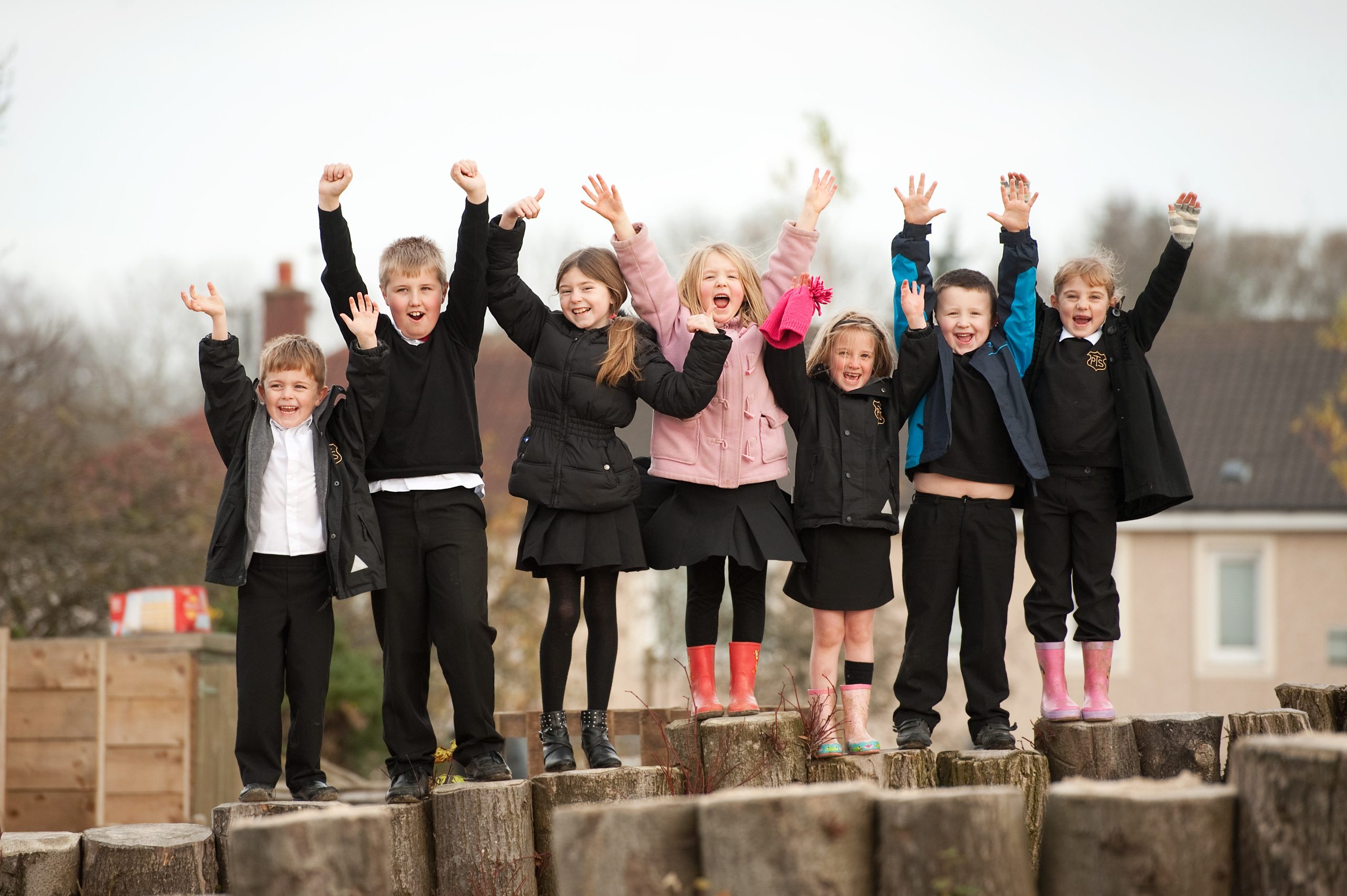 Group of children on tree stumps with their arms raised