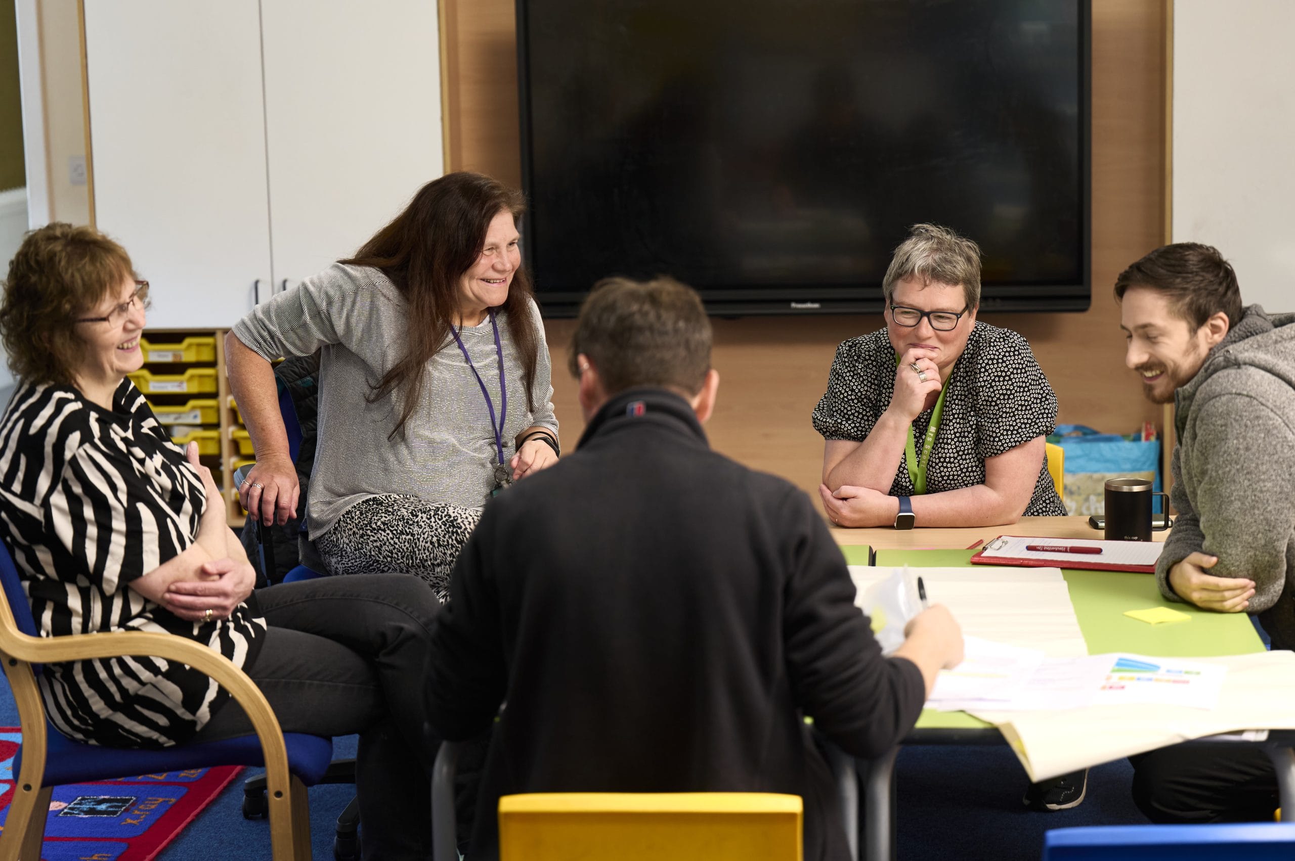 Teachers sit around a table covered with papers, looking happy and engaged