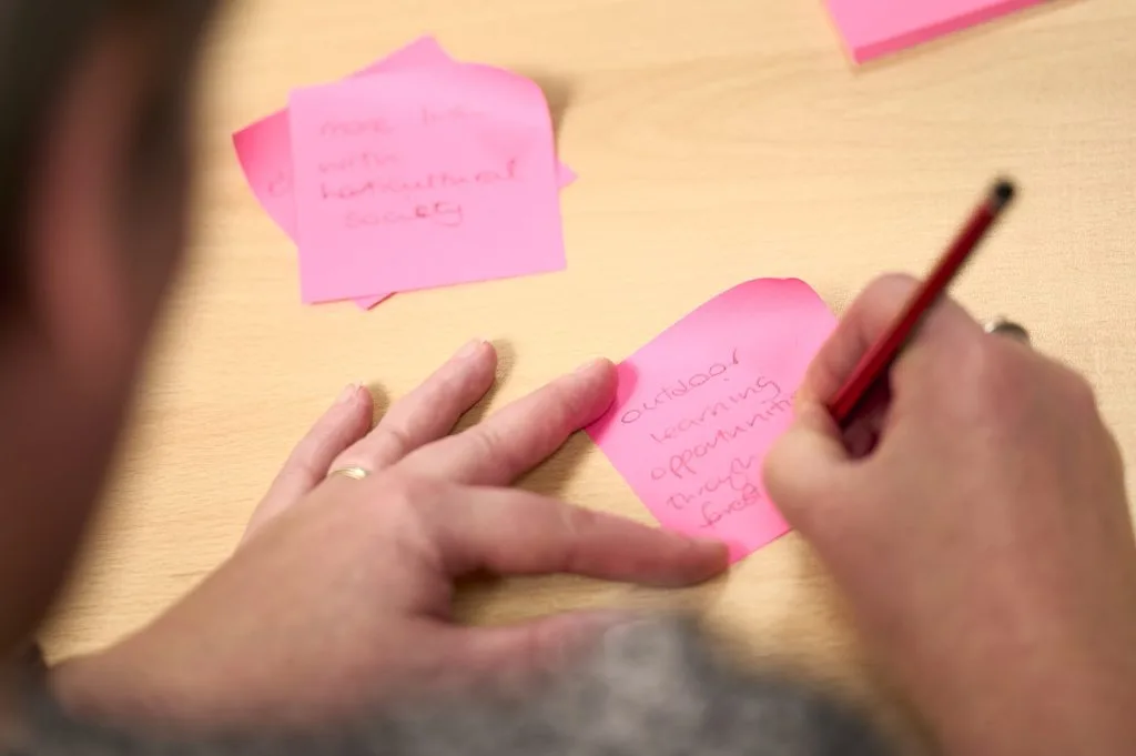 Hands write on pink post-it notes. The words Outdoor Learning are visible